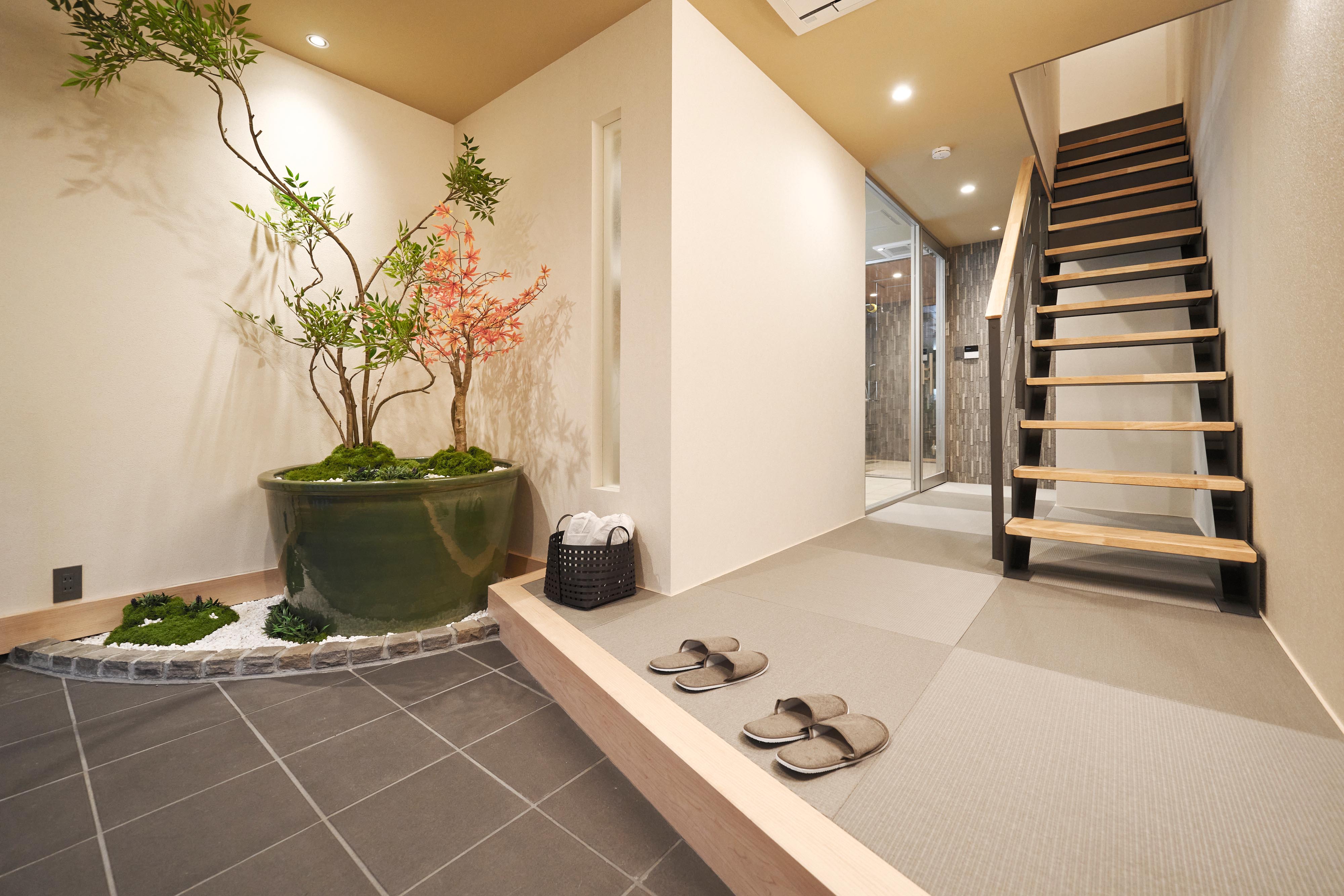 Entrance hall of a SHINKA vacation rental with a potted tree and a wooden staircase